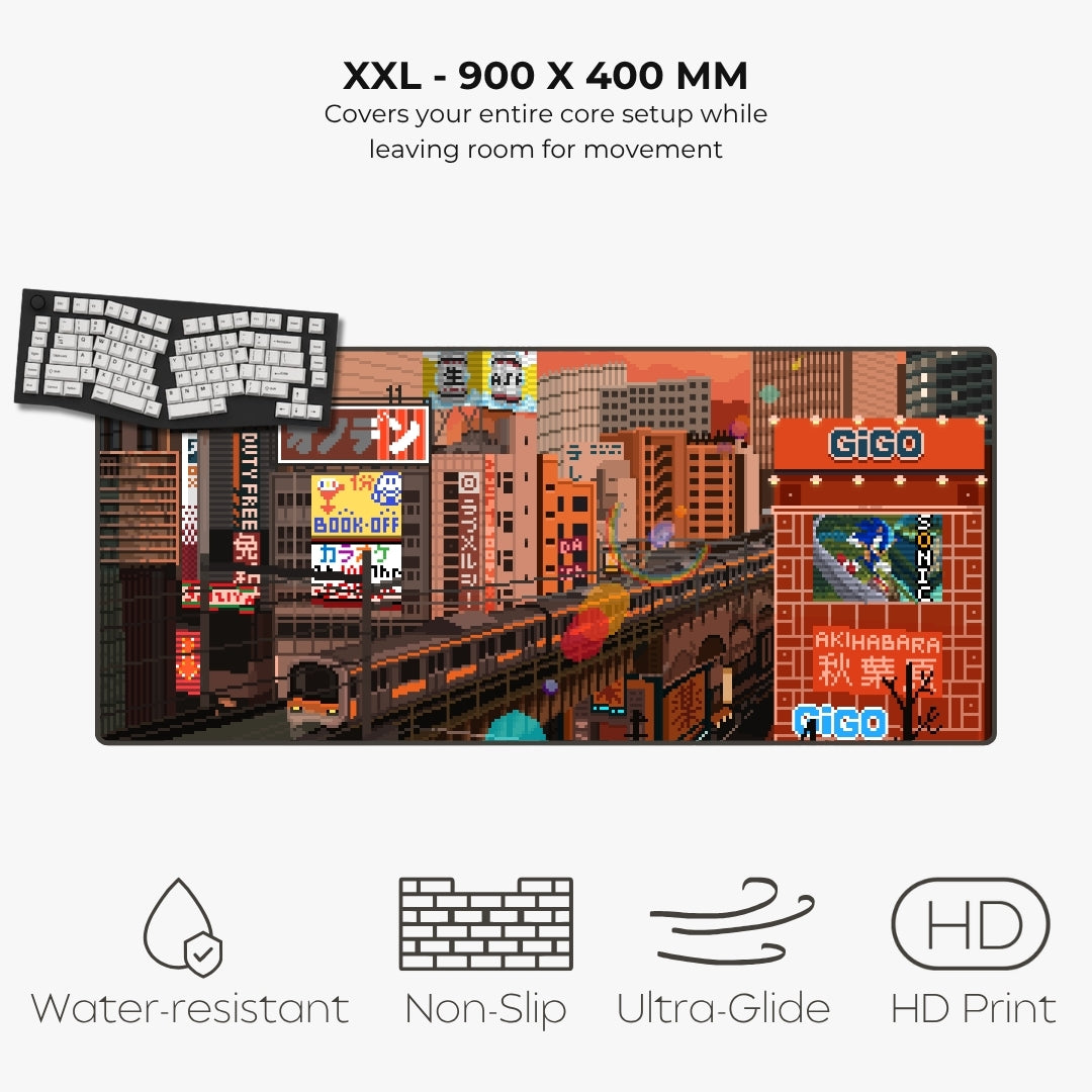 A rectangular gaming playmat featuring a detailed Tokyo cityscape illustration with trains, buildings, and neon signs. The image includes text reading 'XXL - 900 X 400 MM' and feature icons for water-resistant, non-slip, ultra-glide, and HD print.