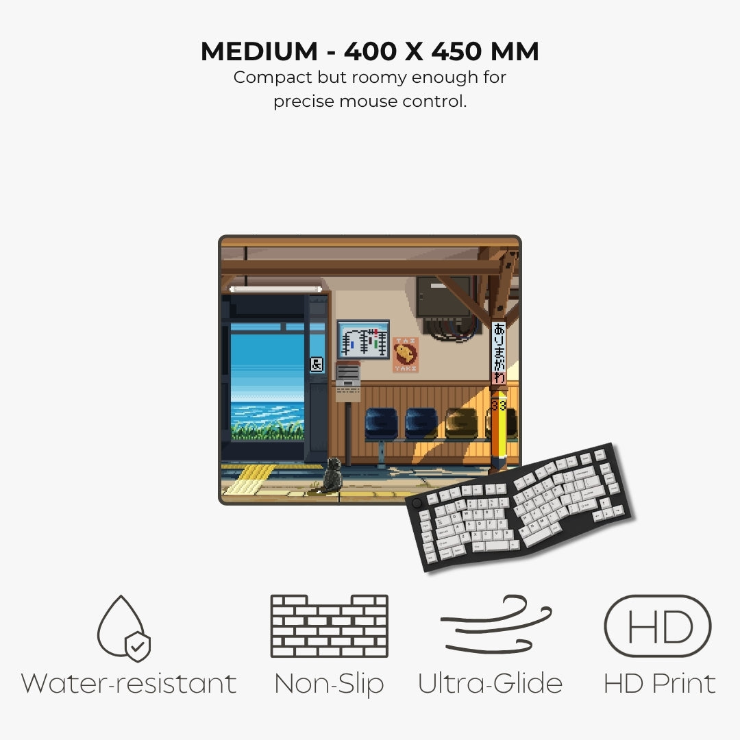 A compact rectangular desk mat featuring an illustrated anime-style train station, with text reading 'MEDIUM - 400 X 450 MM' and feature icons for water-resistant, non-slip, ultra-glide, and HD print.