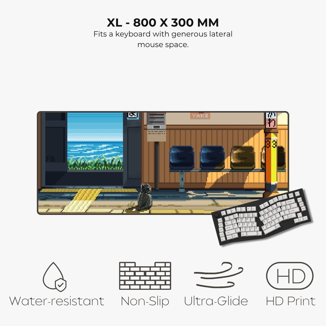 An XL keyboard mat with a pixel-art train station scene, shown with a keyboard on a light gray background. Text at the top reads 'XL - 800 X 300 MM' and describes generous mouse space.