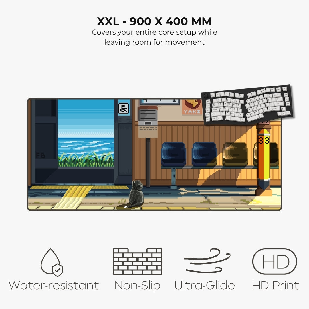 A rectangular anime-style desk mat featuring a train station platform scene with a cat, chairs, and a keyboard, shown on a light gray background with text reading 'XXL - 900 X 400 MM' and feature icons for water resistance, non-slip, ultra-glide, and HD print.