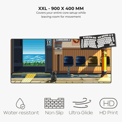 A rectangular anime-style desk mat featuring a train station platform scene with a cat, chairs, and a keyboard, shown on a light gray background with text reading 'XXL - 900 X 400 MM' and feature icons for water resistance, non-slip, ultra-glide, and HD print.