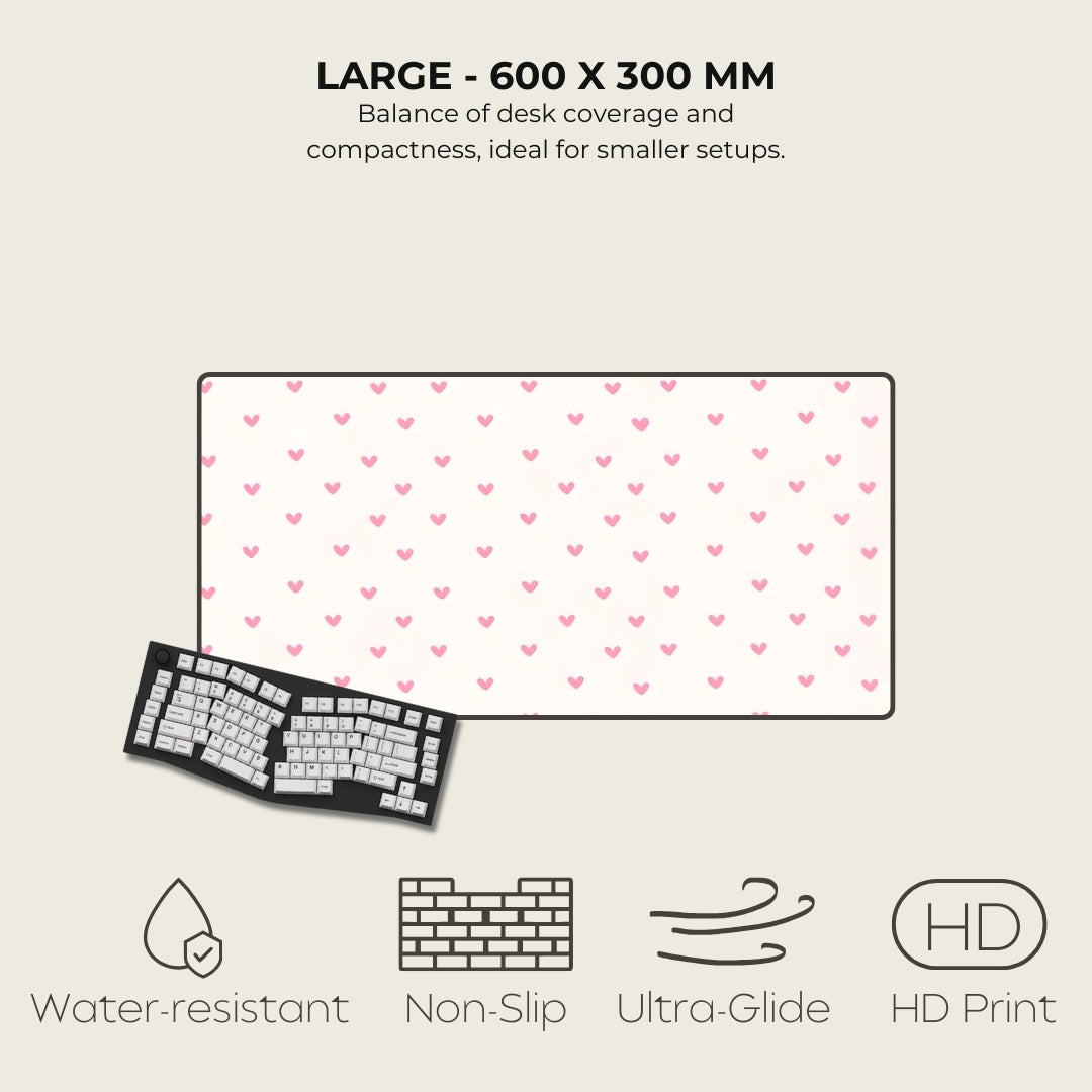 Large desk mat with pink heart pattern, keyboard on the left, text and icons at the bottom.