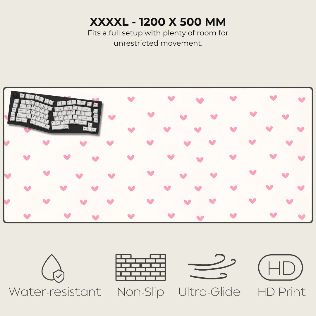 Large desk mat with pink heart pattern, keyboard on left, text and icons at top and bottom.