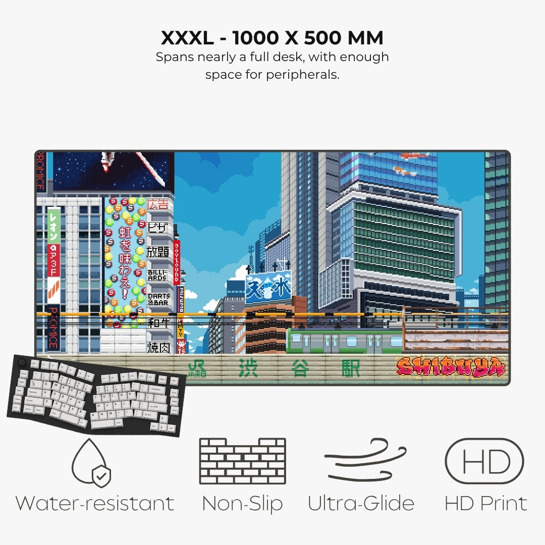 A large desk mat featuring a colorful Japanese cityscape print, shown with a keyboard and mouse placed on it. Text at the top reads 'XXXL - 1000 X 500 MM' and describes the size, with feature icons and labels below: water-resistant, non-slip, ultra-glide, and HD print.