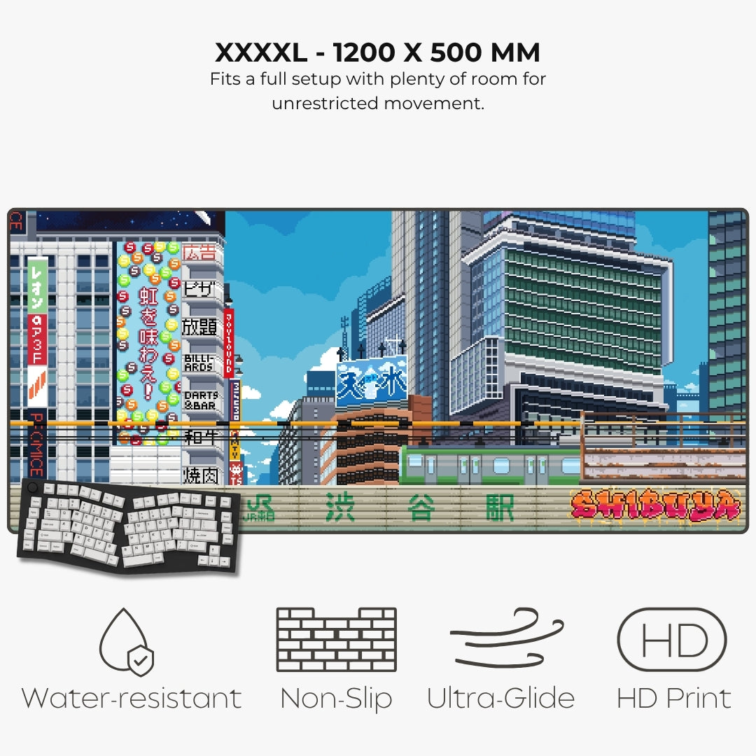 A large rectangular gaming mat shown on a light gray background with text reading 'XXXXL - 1200 X 500 MM' and feature icons for water-resistant, non-slip, ultra-glide, and HD print. The mat features a colorful illustrated cityscape with buildings, a train, and Japanese signage, plus a keyboard and mouse overlay illustration.