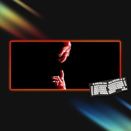 Gaming setup with a rgb mousepad displaying red hands, keyboard, and colorful light effects on a dark background.